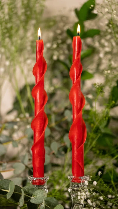 Lit red spiral beeswax candles with greenery
